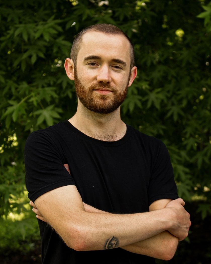 Tom Norman, arms crossed, in front of green foliage